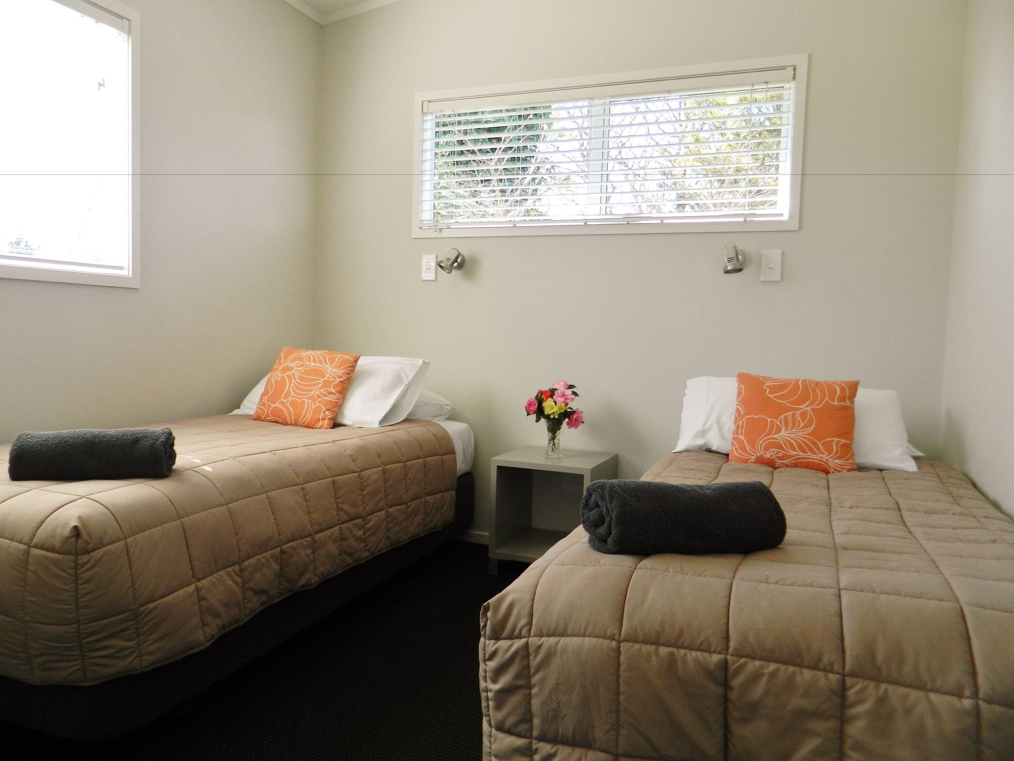 陶波德布雷思汽车旅馆 外观 照片 The image shows a small, cozy room featuring two single beds. Each bed is dressed with a beige quilt and has an orange decorative pillow. There are two rolled towels placed on the beds. A small bedside table is located between the beds, with a vase o