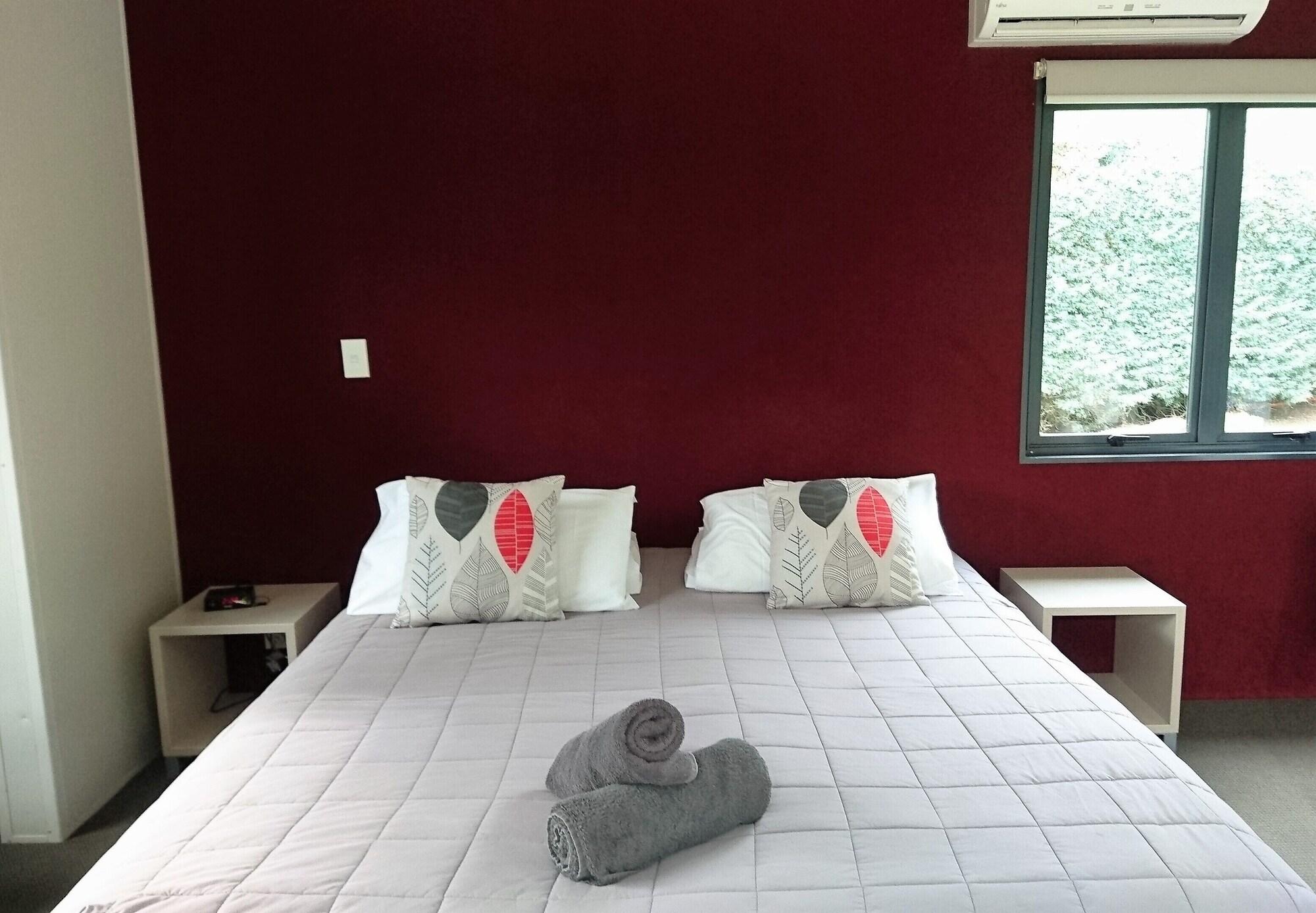 陶波德布雷思汽车旅馆 外观 照片 The photo shows a cozy bedroom featuring a large bed with a light-colored quilt. The bed has two decorative pillows with a simple design on each side. There are two bedside tables, one on each side of the bed. On the bed, there are rolled towels plac