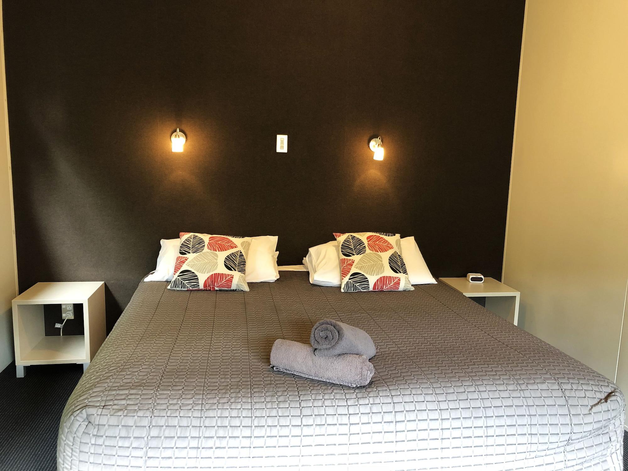 陶波德布雷思汽车旅馆 外观 照片 The photo shows a bedroom with a large bed that has a gray quilted cover and decorative pillows. The walls behind the bed are painted a dark color, and there are two small wall-mounted lamps providing light. On either side of the bed, there are small