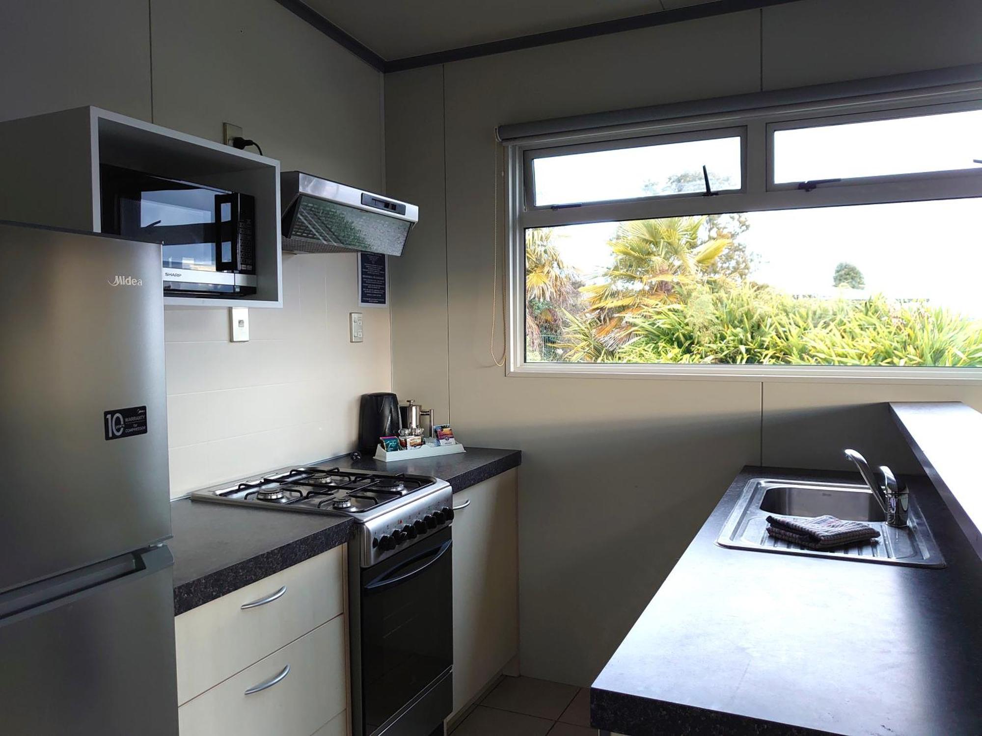 陶波德布雷思汽车旅馆 外观 照片 The photo shows a kitchen equipped with modern appliances. On the left side, there is a refrigerator and a microwave above it. The kitchen features a gas stove with a range hood above. To the right, there is a kitchen sink with a countertop. A window