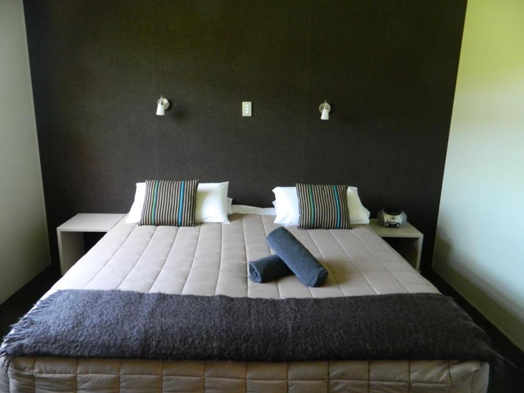 陶波德布雷思汽车旅馆 外观 照片 The photo shows a modern bedroom featuring a large bed with a neutral-colored quilt and decorative pillows. There are two bedside tables on either side of the bed. The wall behind the bed is dark, creating a contrast with the lighter bedding. Additio
