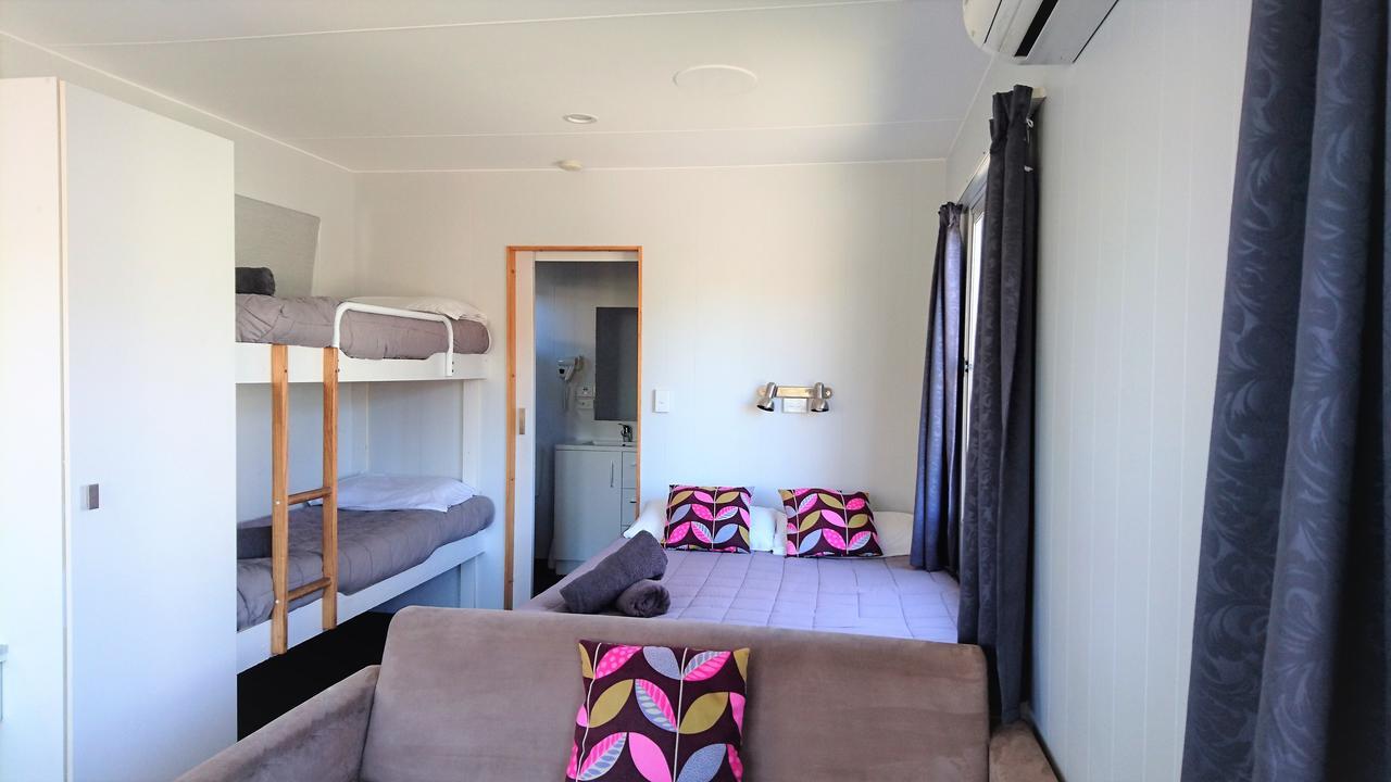 陶波德布雷思汽车旅馆 外观 照片 The photo shows a cozy interior of a room. On the left, there is a bunk bed with two levels, each with gray bedding. In the middle, there is a doorway leading to another space, which appears to be a bathroom. To the right, there is a comfortable couc