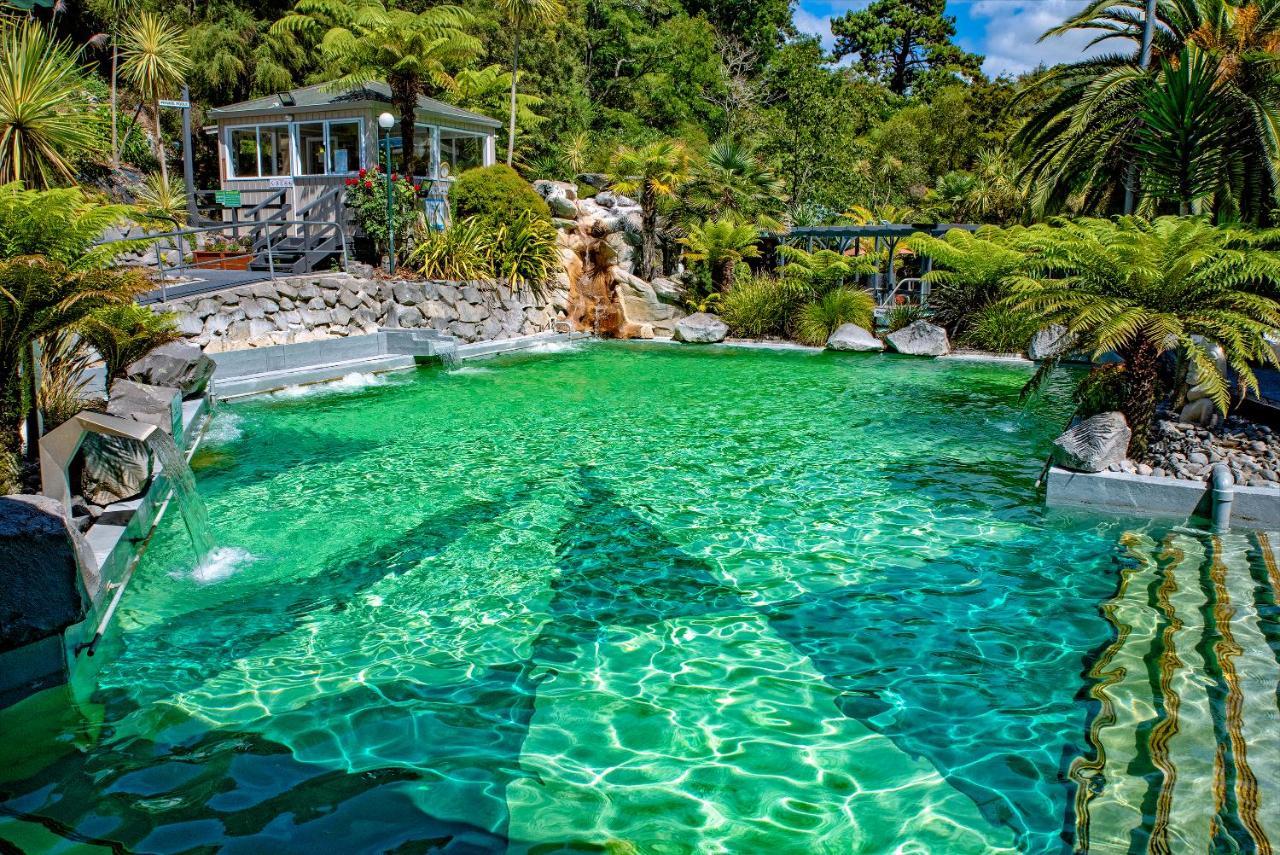 陶波德布雷思汽车旅馆 外观 照片 The photo showcases a vibrant, natural-looking pool with crystal-clear, turquoise water. Surrounding the pool are lush green plants and palm trees, creating a tropical atmosphere. In the background, there is a white building, possibly a facility or a